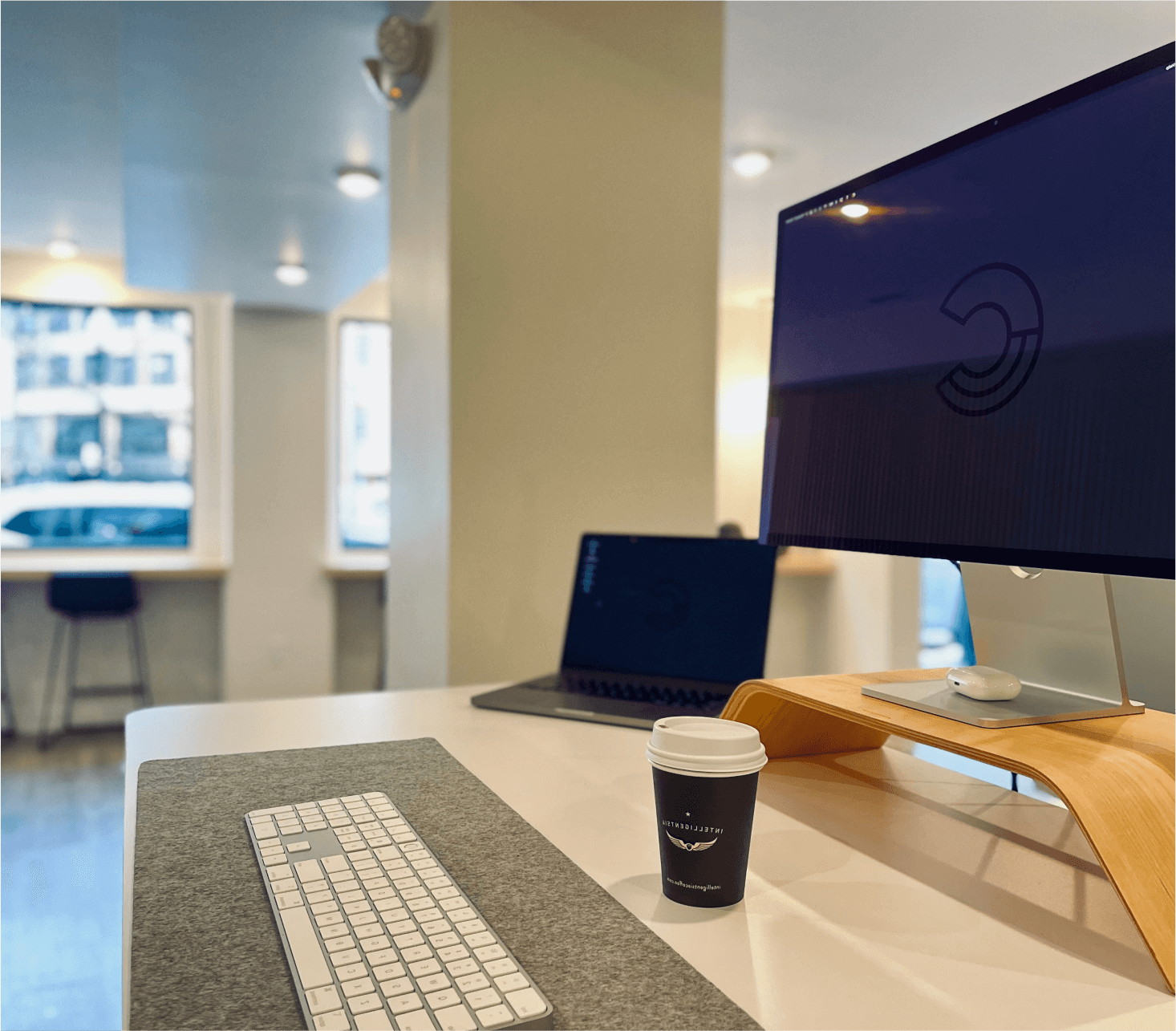 Close-up shot of a desk setup in the Craft Boston office featuring a desktop monitor, keyboard, laptop, and cup of coffee.